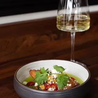 Green dish with fried item, cilantro, cheese, and white wine.