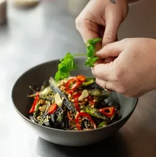 Fair hand garnishes colorful food bowl with fresh green cilantro.