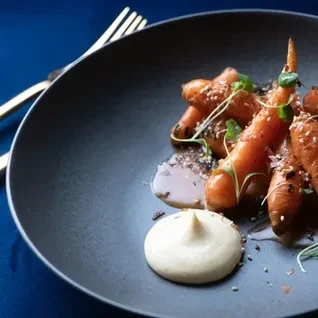 Meticulously plated roasted carrots, dark sauce, creamy purée, and herbs.