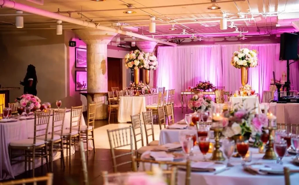 Elegant event space with decorated tables, floral centerpieces, and pink lighting.