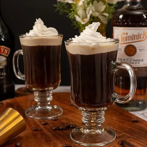 Two Irish coffees with whipped cream, Baileys and whiskey bottles.