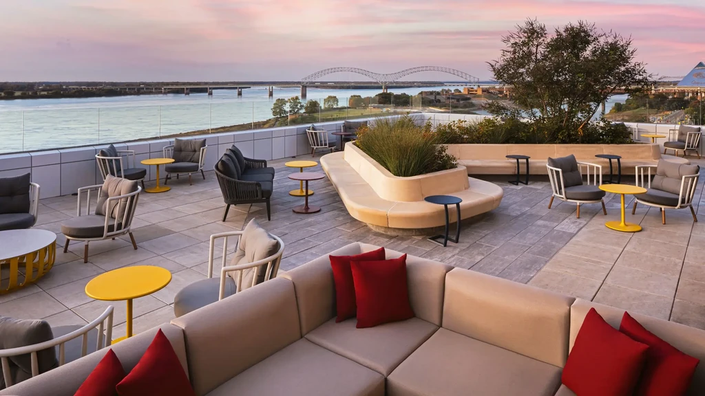 Modern rooftop patio with colorful furniture, river and city at sunset.