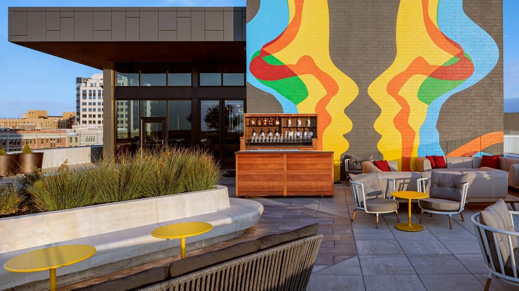 Modern rooftop patio bar with colorful mural, seating, and city view.
