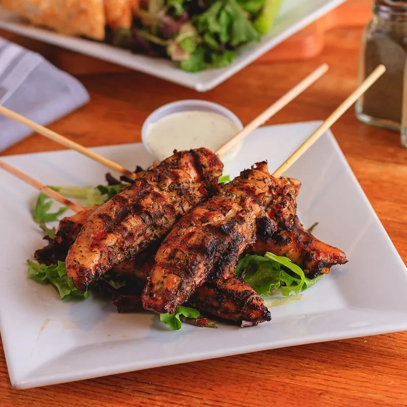 Golden-brown grilled chicken skewers with greens and white dipping sauce.