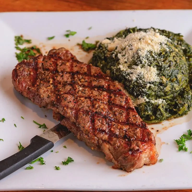 Grilled steak with creamed spinach and cheese on a white plate.