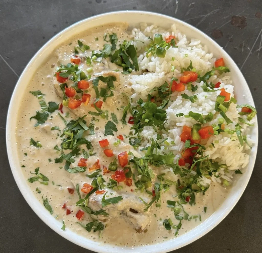 Overhead: bowl of creamy stew, white rice, green herbs, and red garnish.