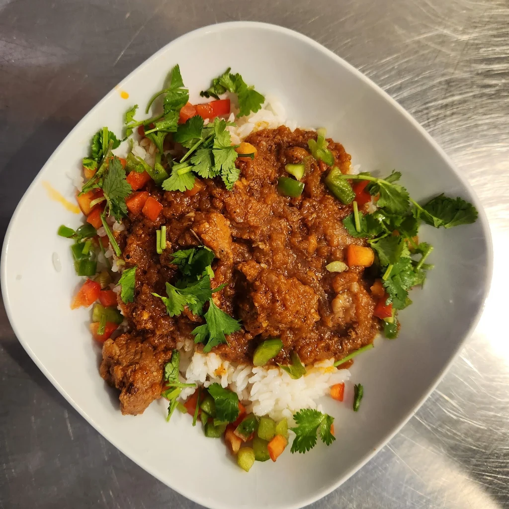 White rice with chunky reddish-brown stew, garnished with cilantro and peppers.