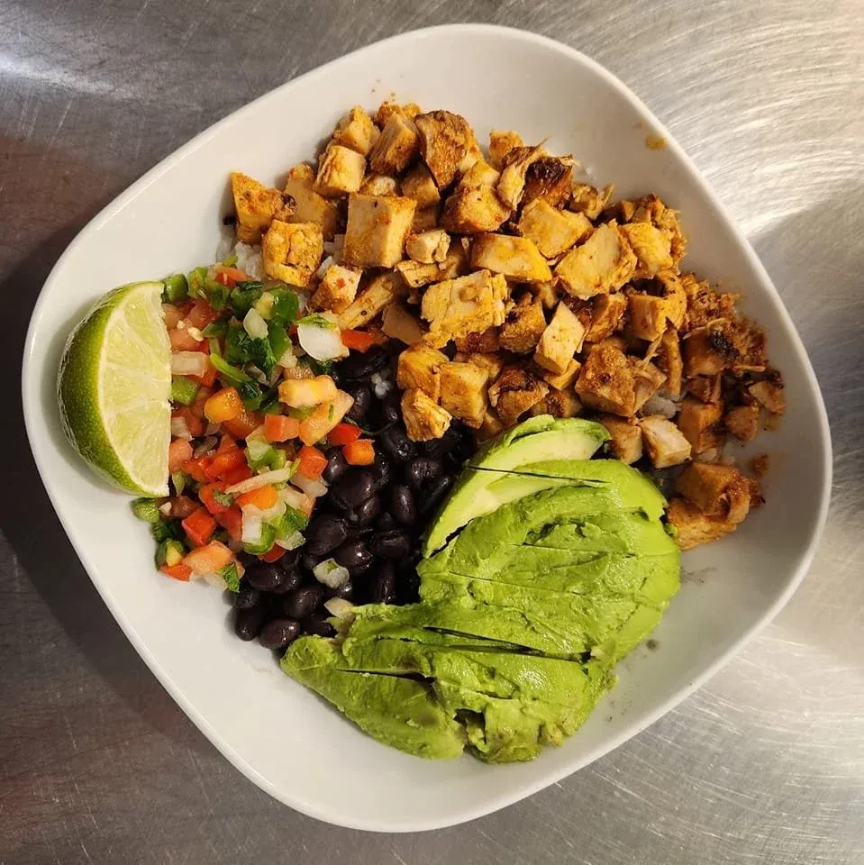 Overhead view of a colorful chicken burrito bowl with avocado and lime.