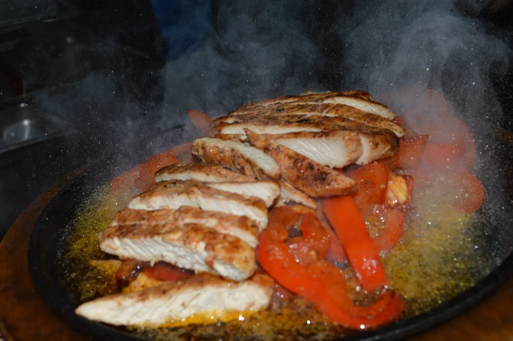Sizzling grilled chicken and red peppers on a cast iron skillet.