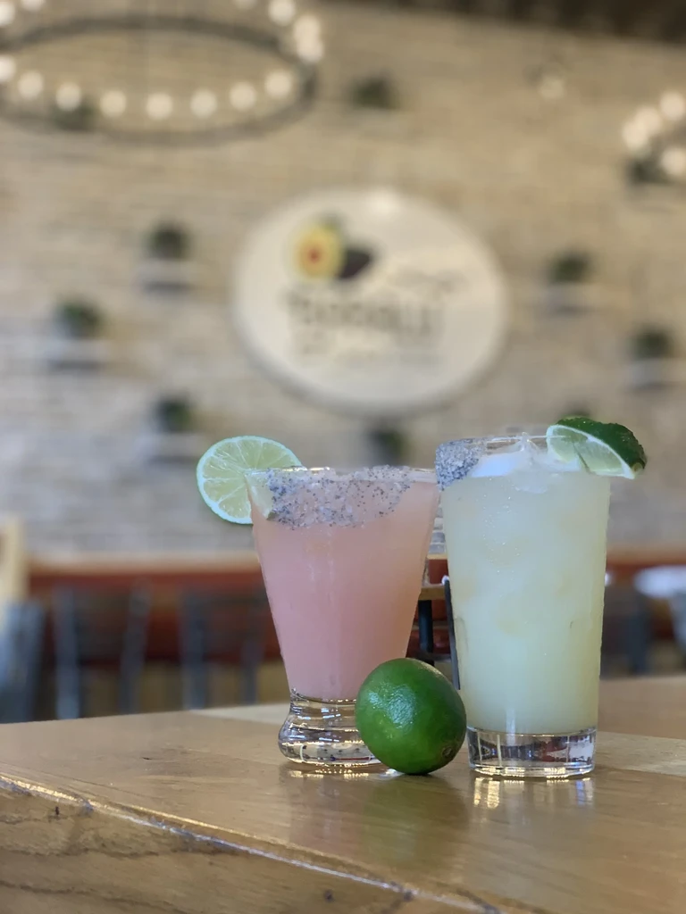 Two garnished drinks and a lime on a wooden table, blurred background.
