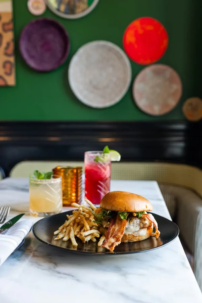 Gourmet burger, fries, and colorful cocktails on a marble restaurant table.