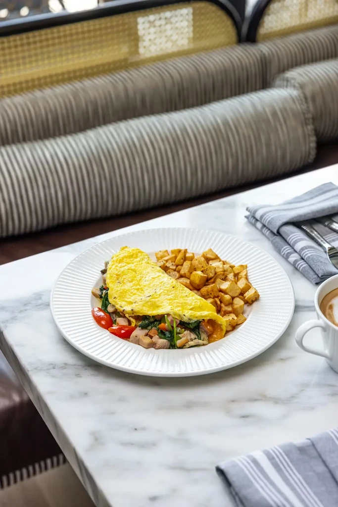Folded omelet, home fries, and latte on a white marble restaurant table.
