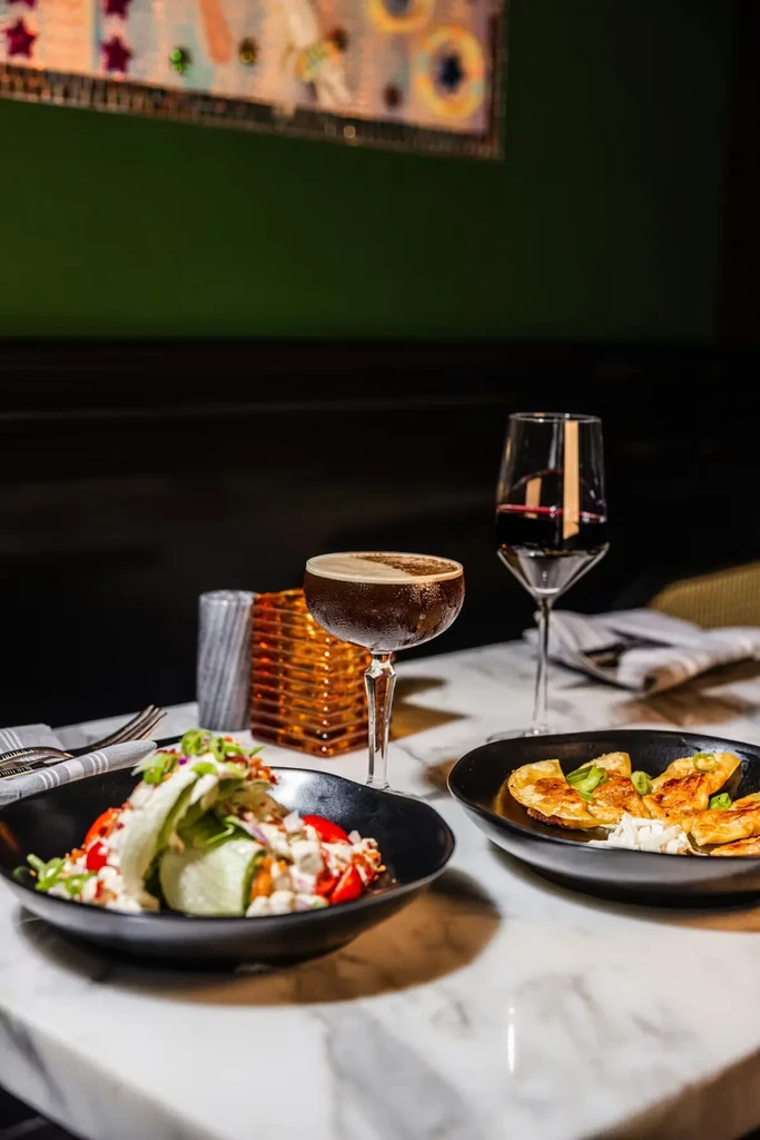 Salad, dumplings, cocktail, and red wine on an upscale marble table.