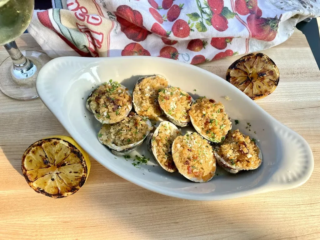 Golden-brown baked clams, charred lemons, and wine on a sunny table.