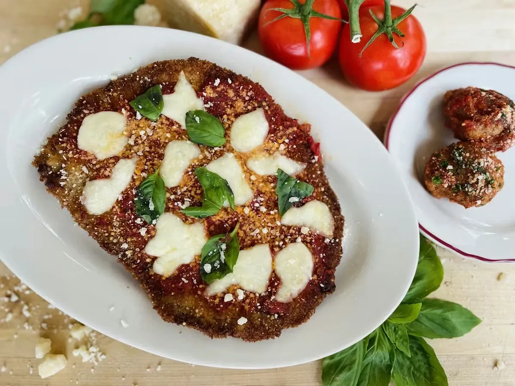 Crispy parmigiana cutlet, meatballs, and fresh ingredients on a wooden board.