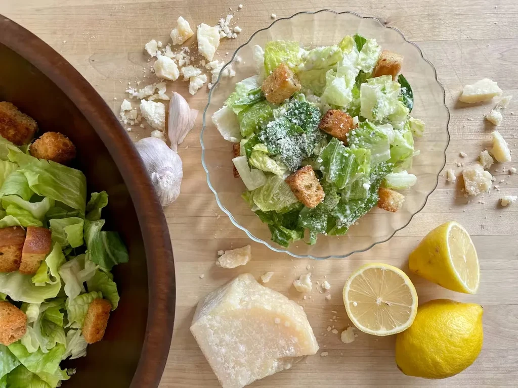 Overhead shot of Caesar salad, lettuce, croutons, Parmesan, garlic, lemons.