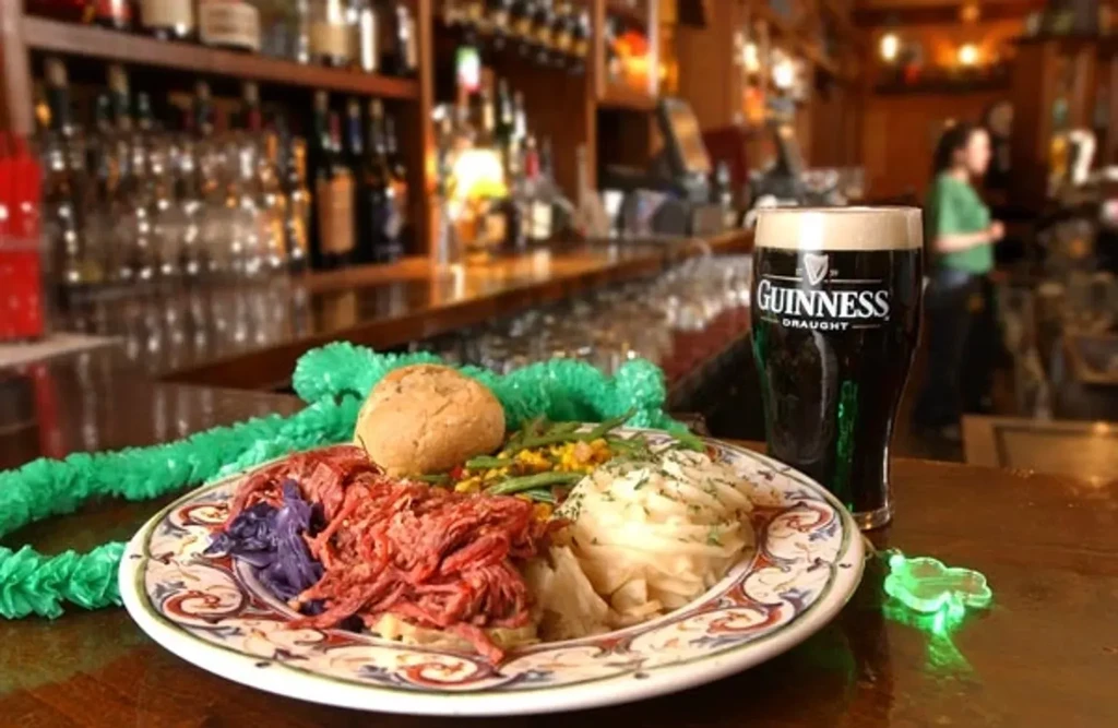 Guinness pint, corned beef meal, and shamrock on an Irish pub bar.