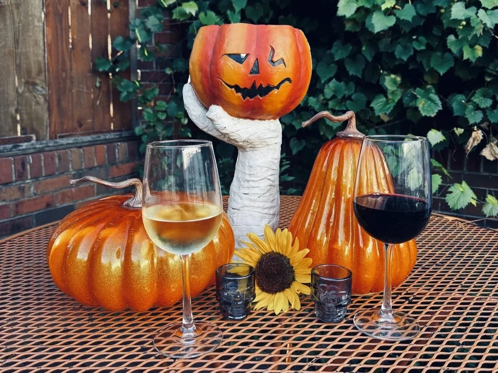 Wine glasses on a Halloween patio with pumpkins, mummy hand, and skulls.