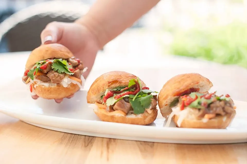 Three golden buns with meat, vegetables, red sauce, one held.
