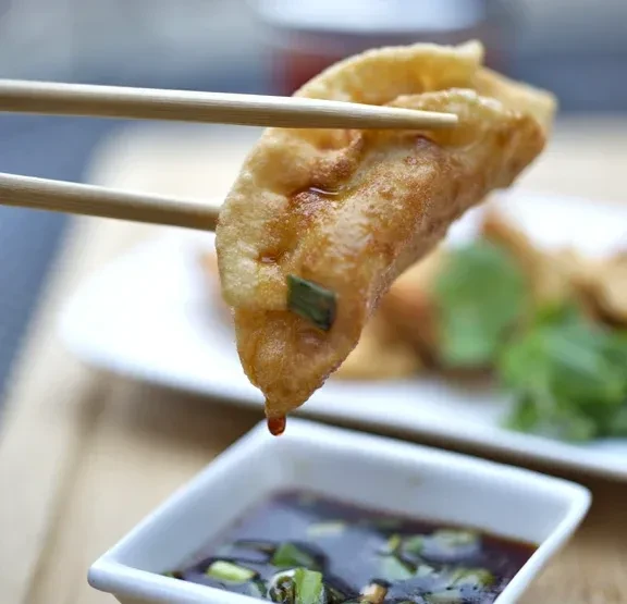 Golden-brown, crispy fried dumpling held by chopsticks, dripping sauce.