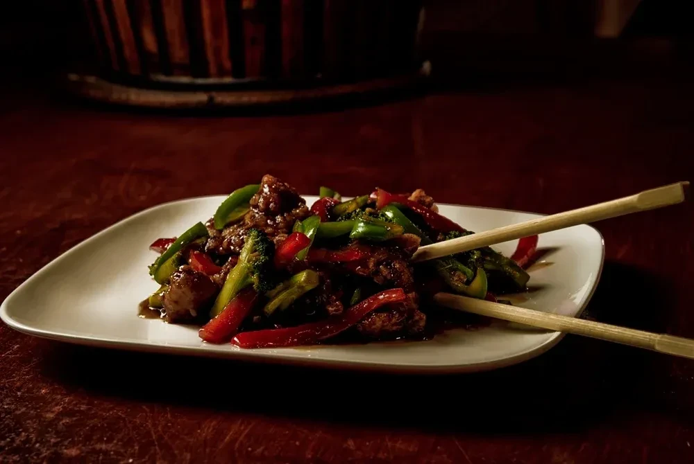 Stir-fry with beef, broccoli, bell peppers, and chopsticks on a white plate.
