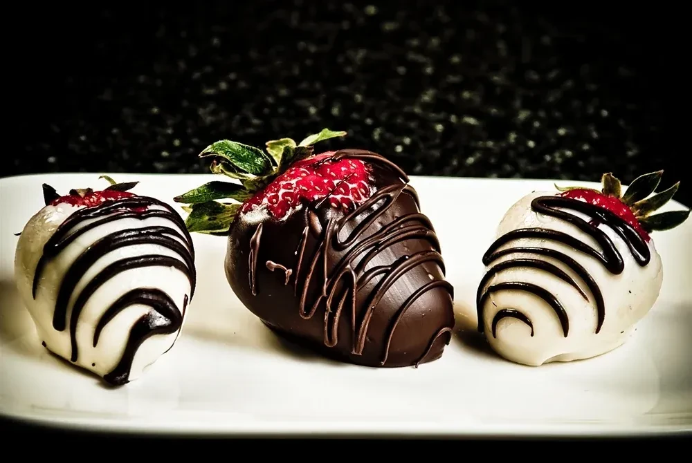 Three chocolate-covered strawberries: one dark, two white, on a white plate.