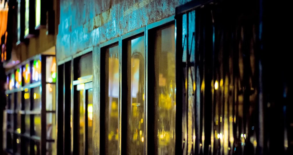 Weathered building facade at night, warm light reflects in windows.