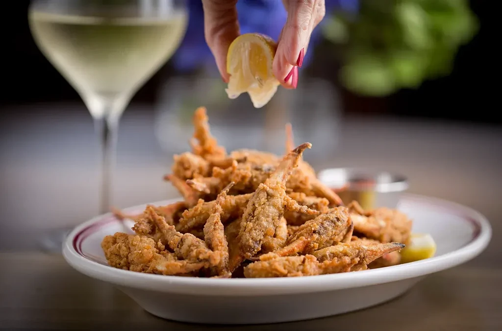 Hand with red nails squeezing lemon over crispy fried seafood.