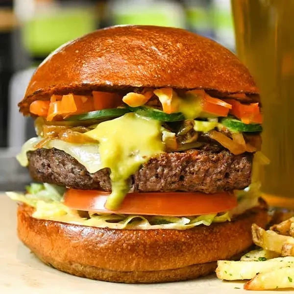 Close-up gourmet burger with melted cheese, tomato, lettuce, fries, and beer.