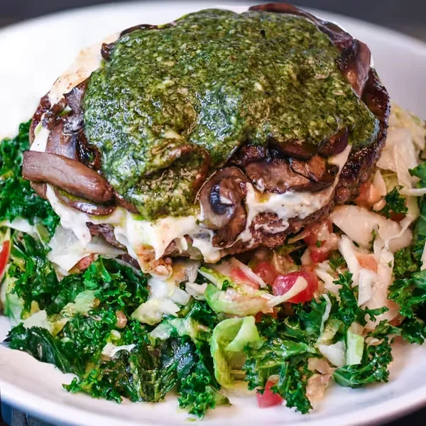 Generously portioned open-faced patty with melted cheese, mushrooms, pesto, and greens.