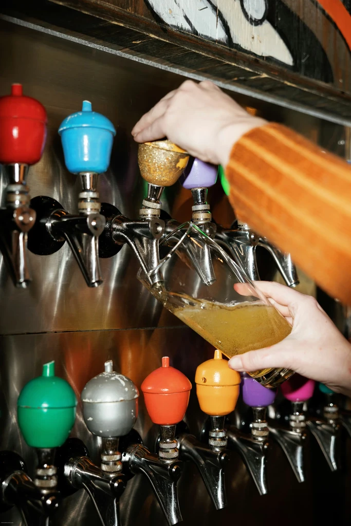 Hands pouring a drink from colorful acorn-handled bar taps.
