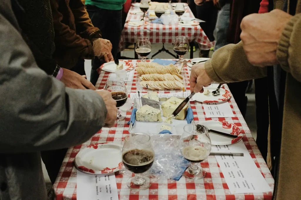 Close-up of hands serving cheese and beer on a checkered table.