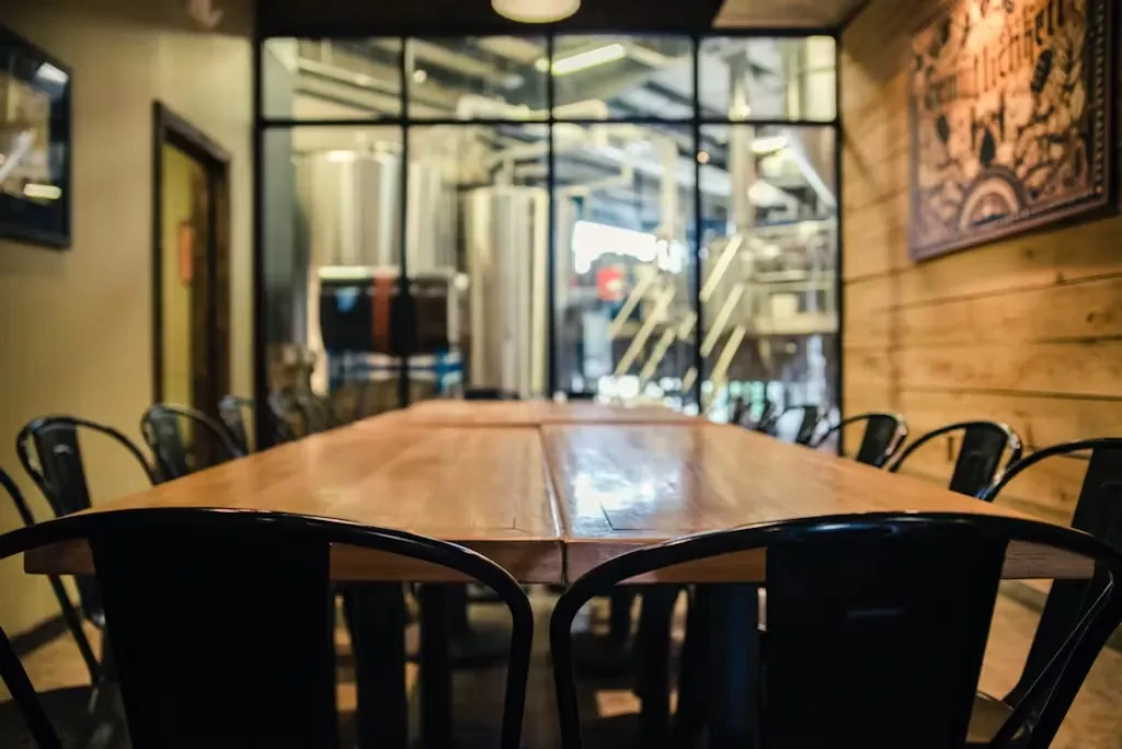 Empty brewery taproom with communal table and stainless steel tanks.
