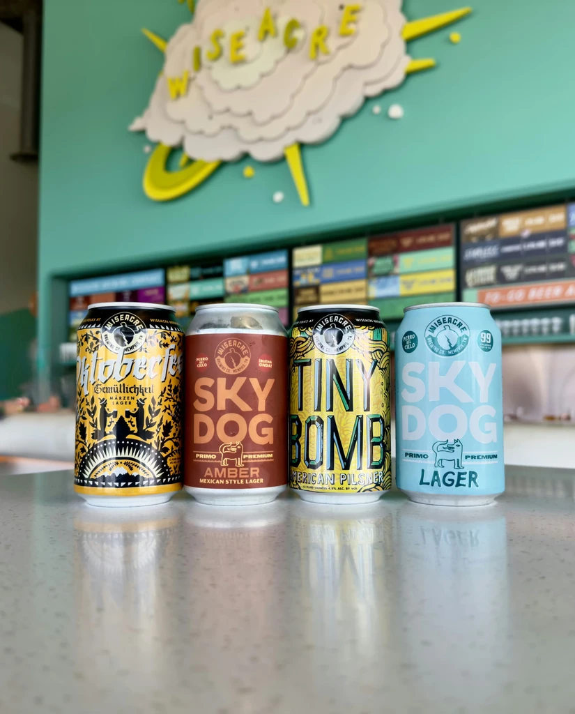 Four Wiseacre beer cans on a reflective counter in a brewery.