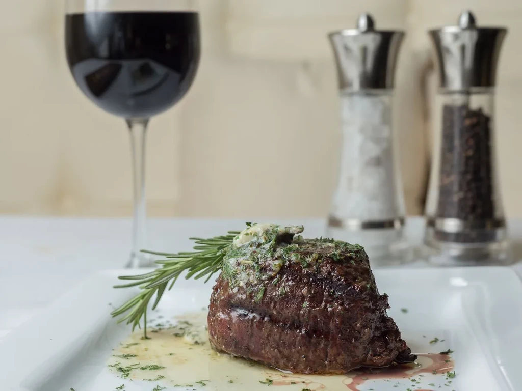 Cooked steak on white plate with herb butter and rosemary sprig.