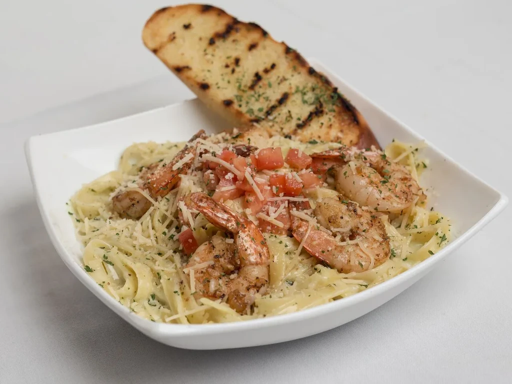 Creamy shrimp pasta topped with tomatoes, Parmesan, and grilled garlic bread.