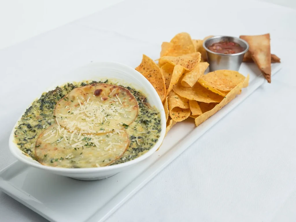 Spinach artichoke dip with melted cheese, tortilla chips, salsa, and pastries.
