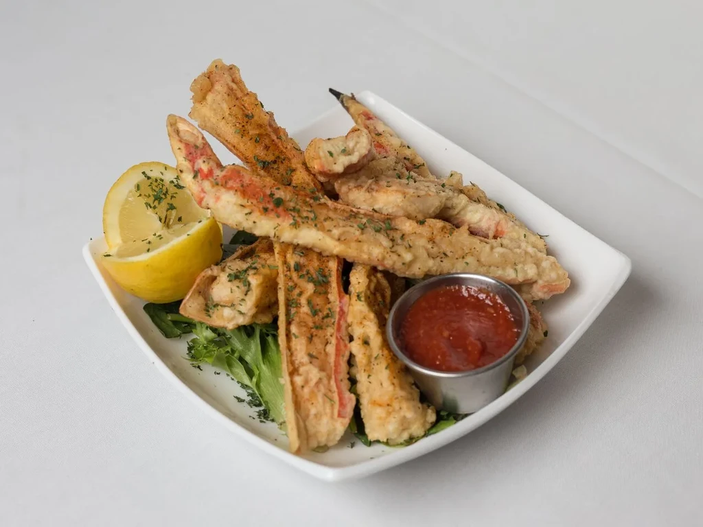 Golden deep-fried seafood, lemon, herbs, and dipping sauce on a white plate.