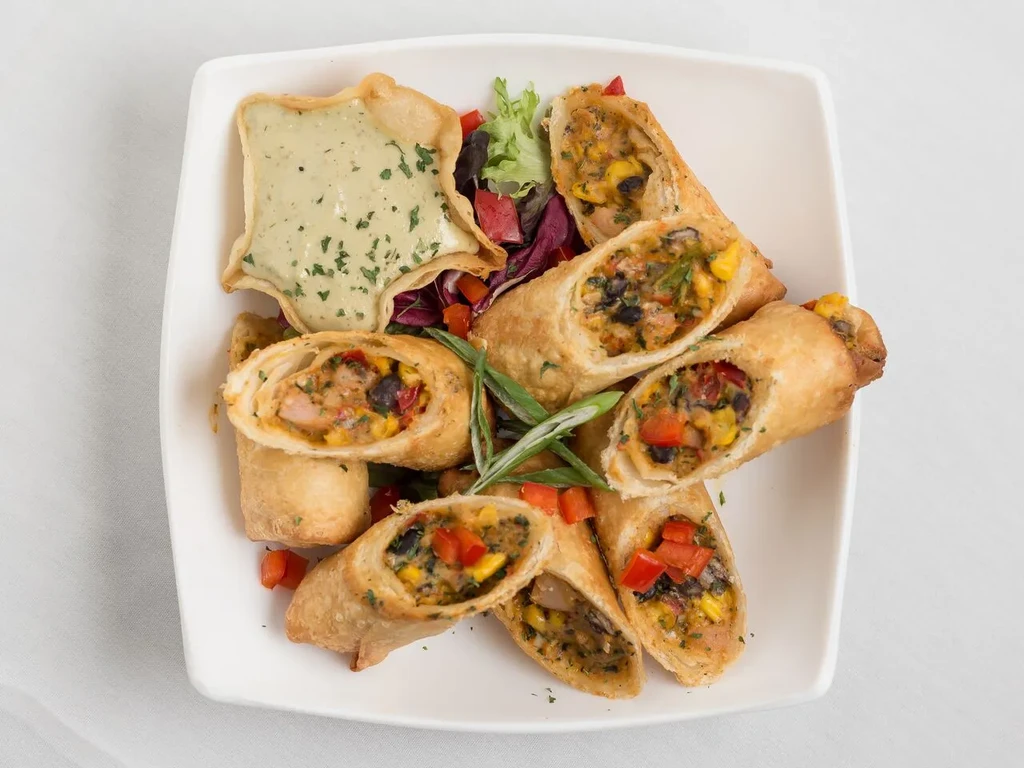 Fried rolls showing bean, corn, pepper filling with greens and green dip.