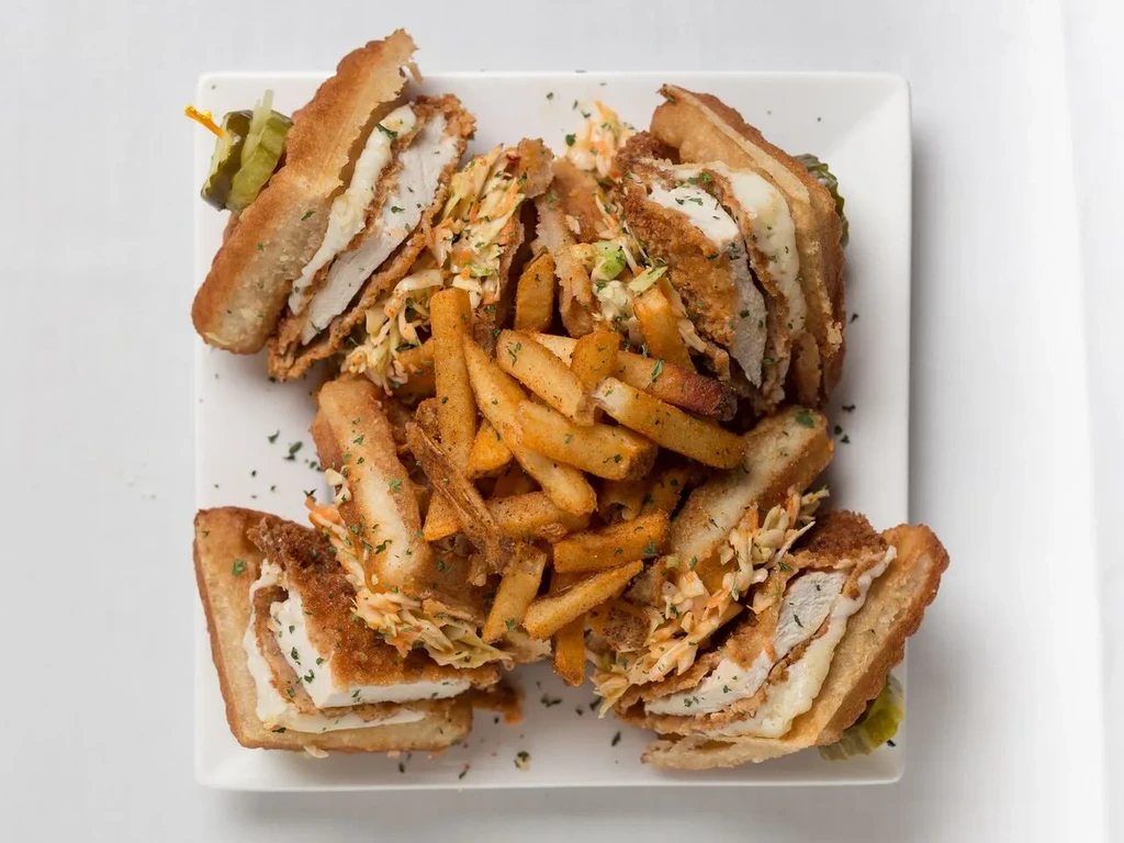 Fried chicken sandwich quarters, fries, and pickles on a white plate.