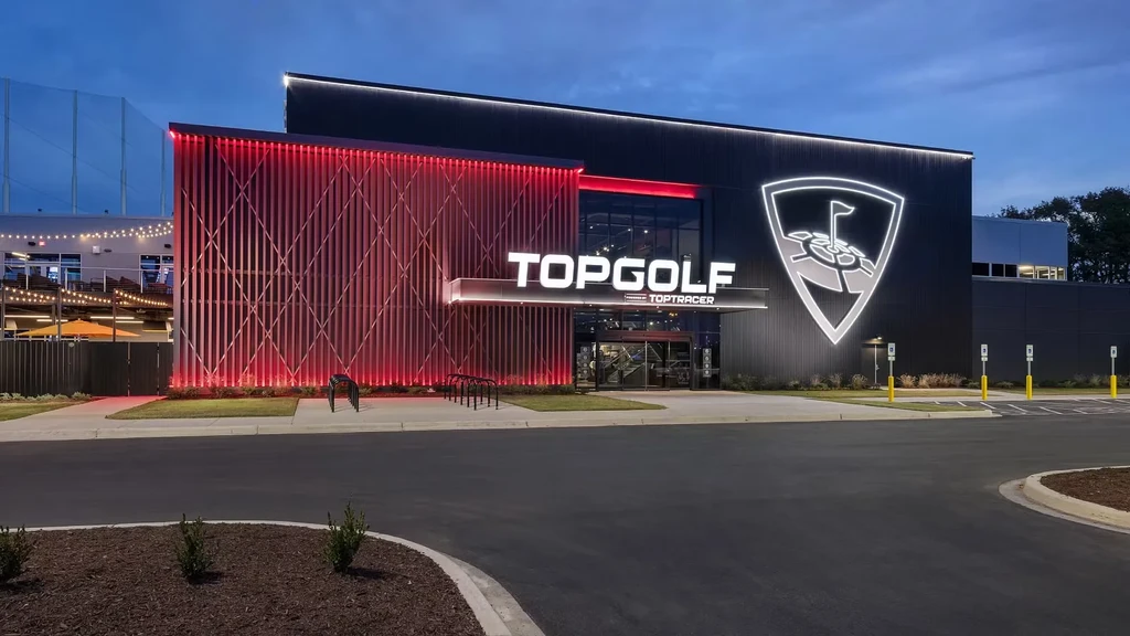 Modern illuminated Topgolf building exterior at dusk with golf netting.