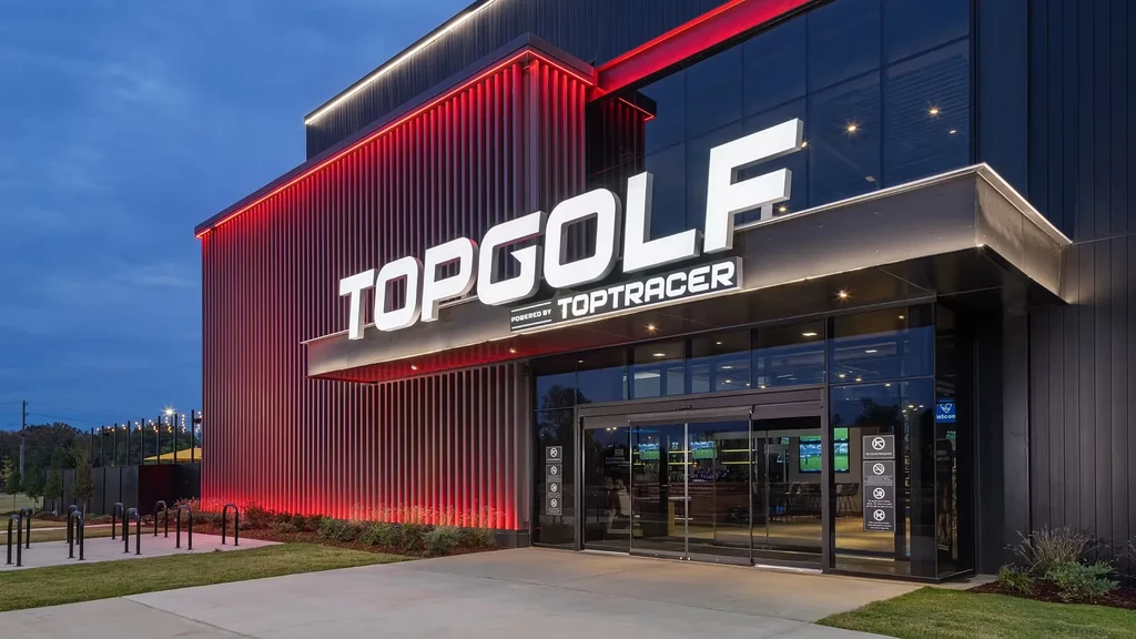 Modern Topgolf building exterior at night, brightly lit red and white.