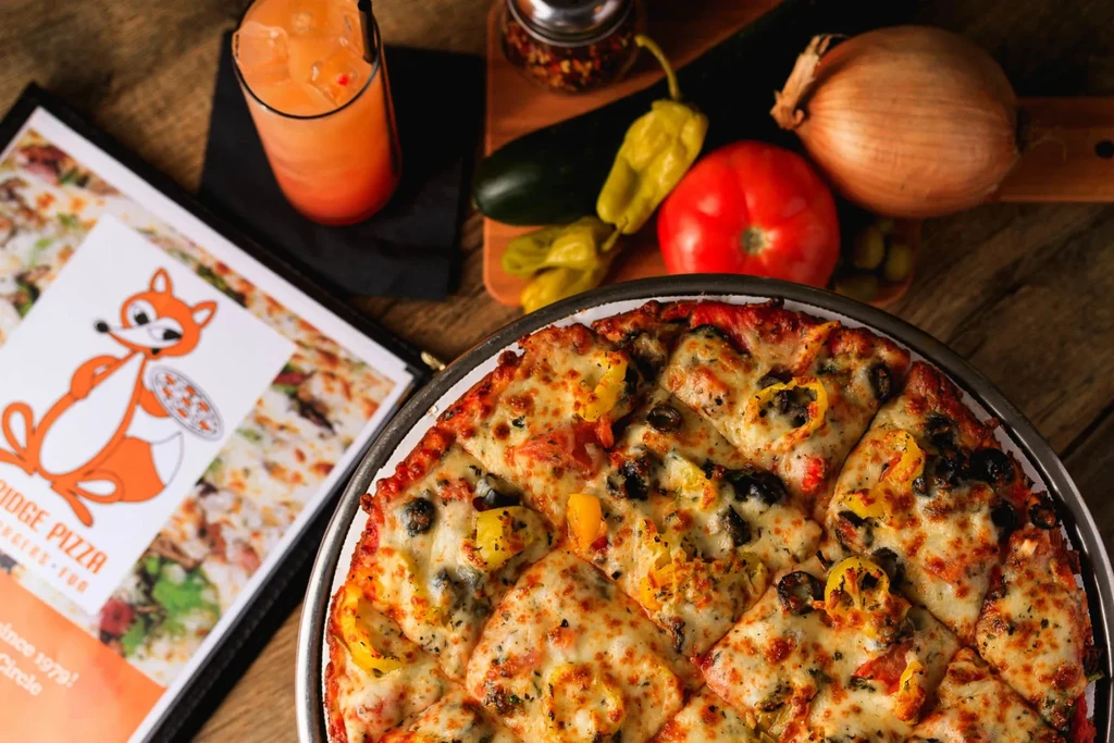 Overhead pizza with olives, bell peppers, surrounded by fresh ingredients.