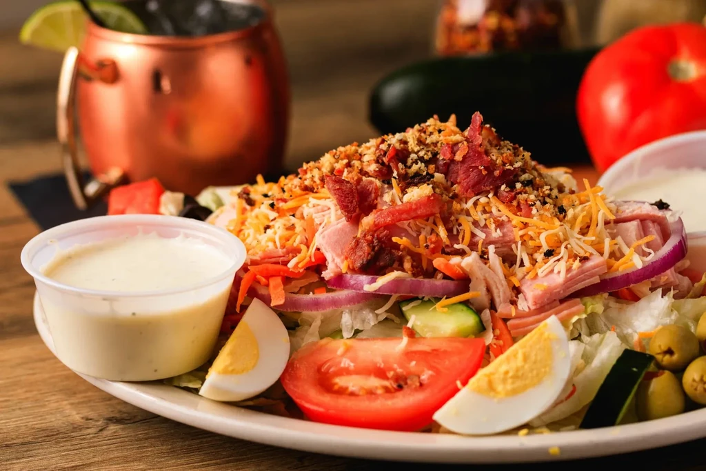 Hearty salad with ham, cheese, bacon, egg, vegetables, croutons, and dressing.