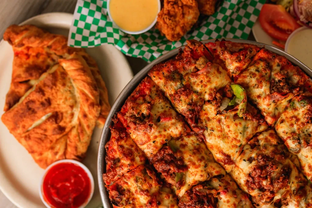 Overhead photo of pizza, fried chicken, calzone, and dipping sauces.