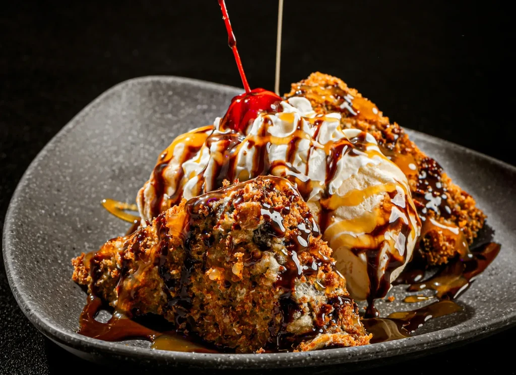 Fried dessert with whipped cream, chocolate, caramel, and a cherry.