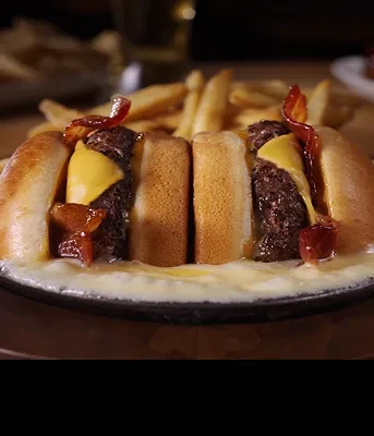 Skillet of cheesy bacon sliders with a side of french fries.