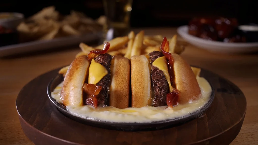 Skillet of bacon cheeseburger sliders in cheese sauce with fries.