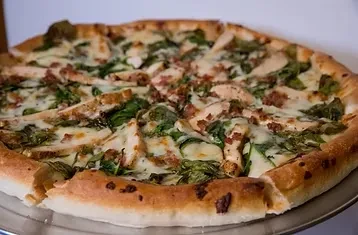 Freshly baked, sliced pizza with chicken, spinach, mozzarella, bacon.