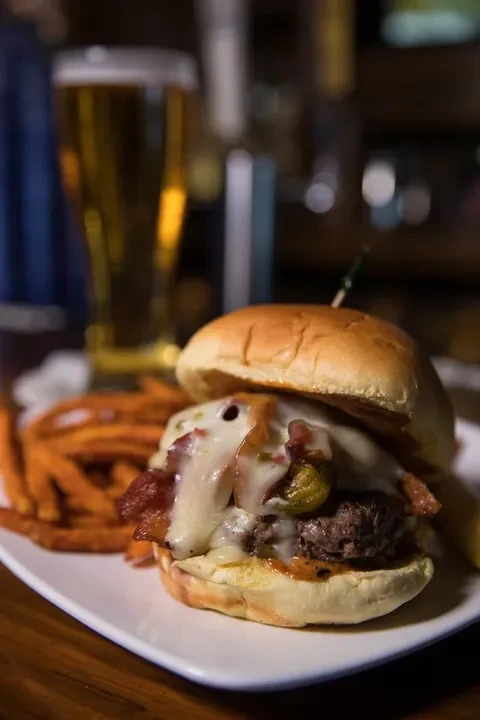 Burger with bacon, melted cheese, jalapeños, and sweet potato fries.